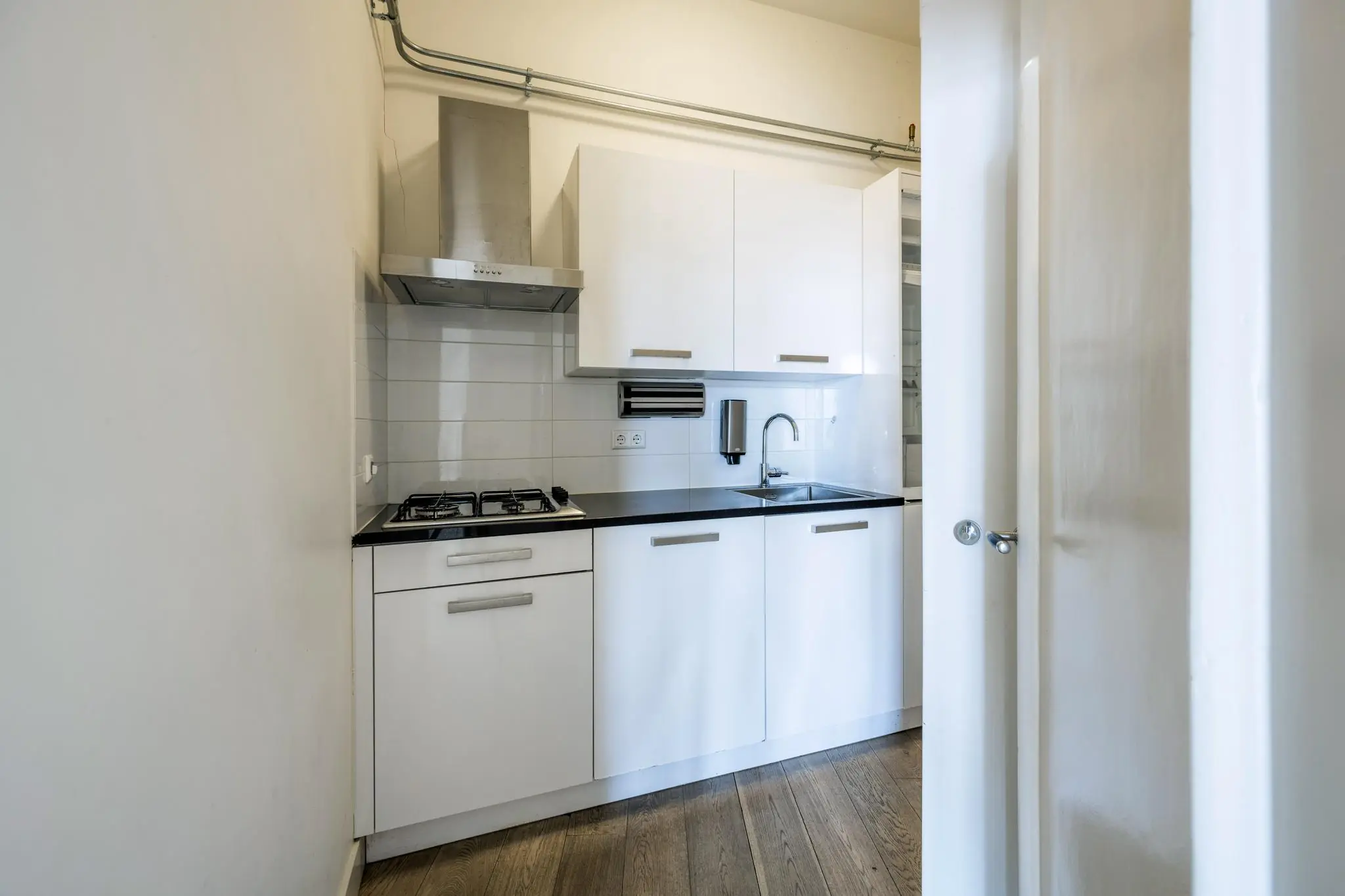 Moderne, compacte witte keuken aan de De Ruijterkade met gaskookplaat, afzuigkap en houten vloer.